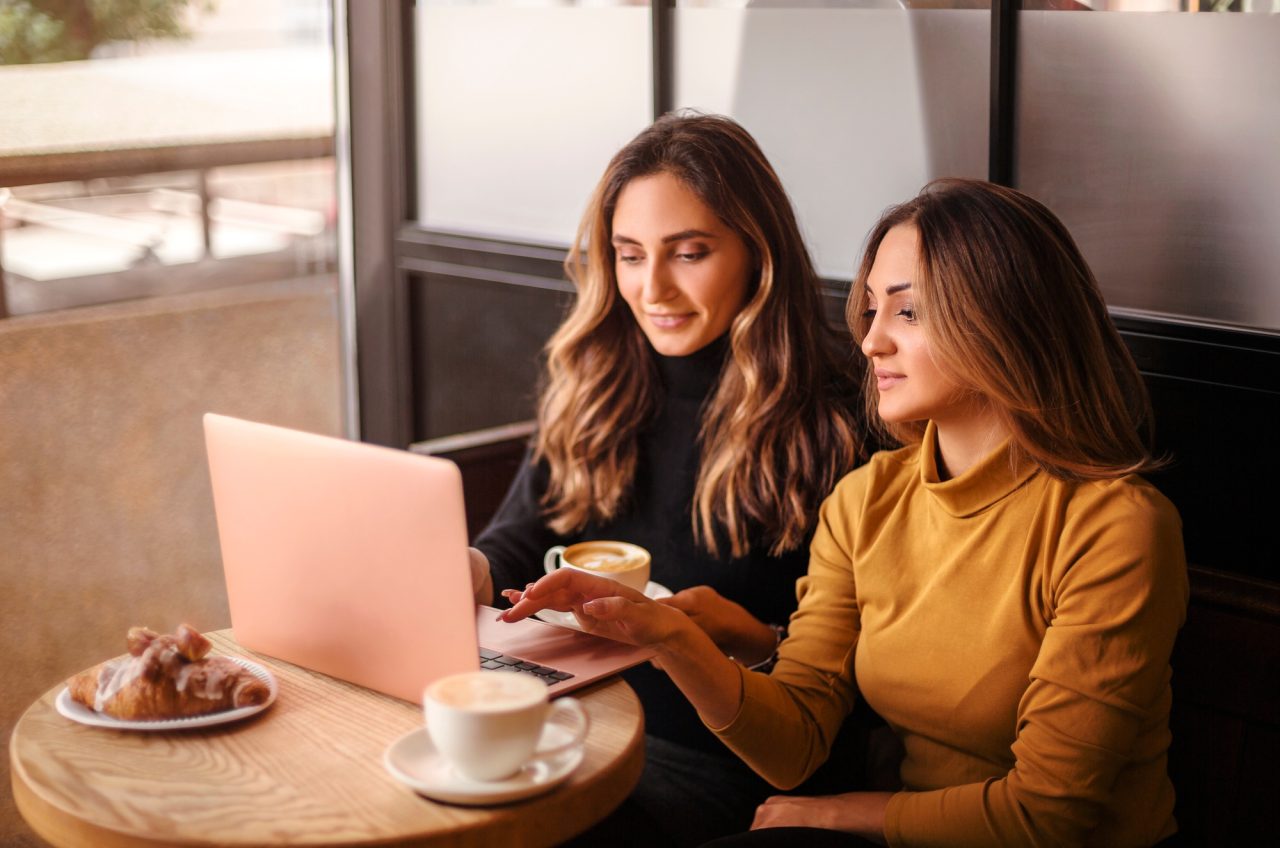 two young happy attractive women business partners using at laptop at meeting in cafe 1